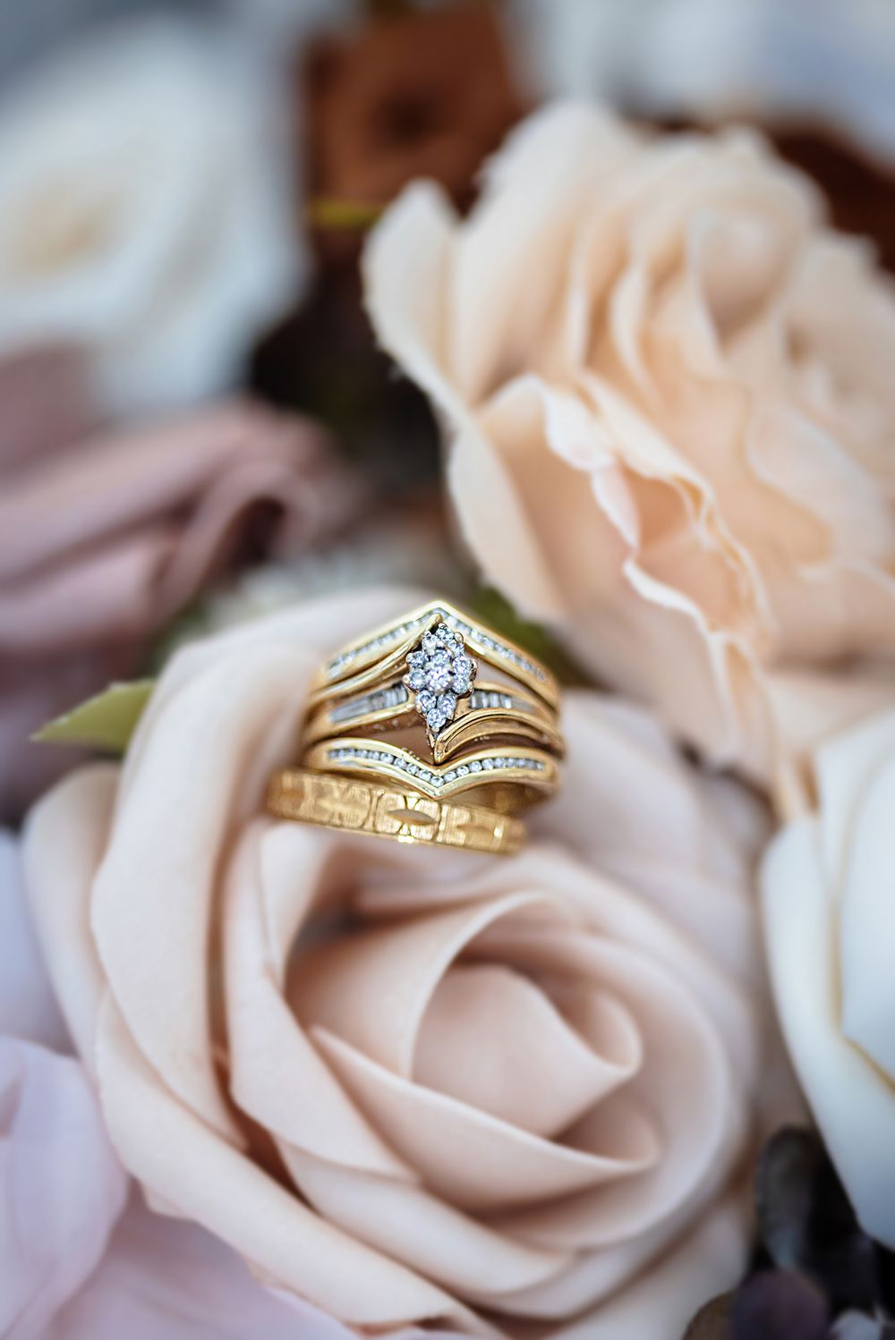 Sparkling diamond engagement ring nestled among soft blush pink roses in a romantic wedding detail shot.