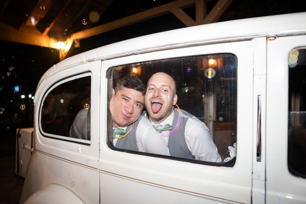 Happy couple departing in a vintage white car at the end of their wedding celebration.