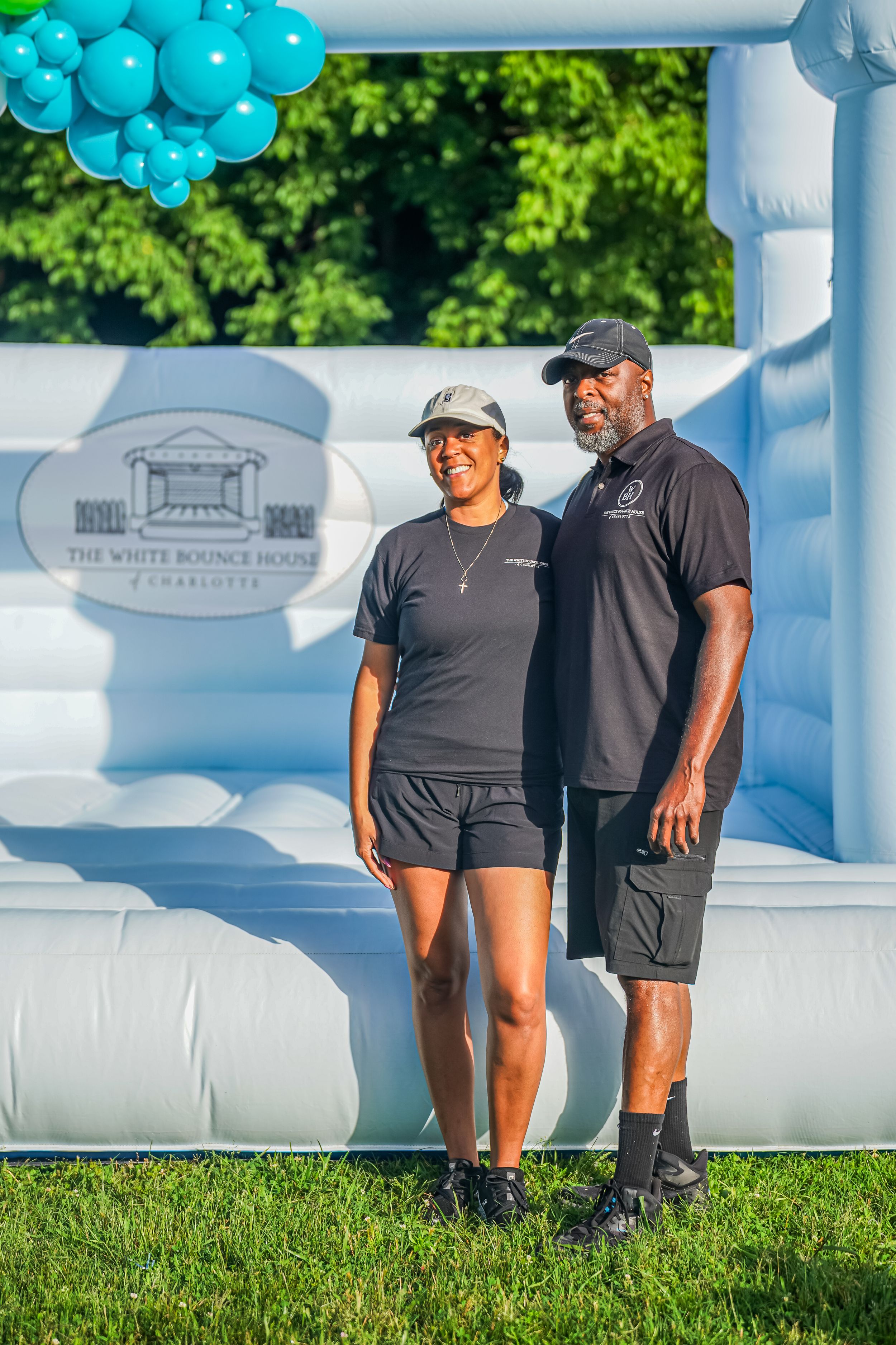 Two people stand together by an inflatable structure with a White House Summit logo and blue balloons at an outdoor event.