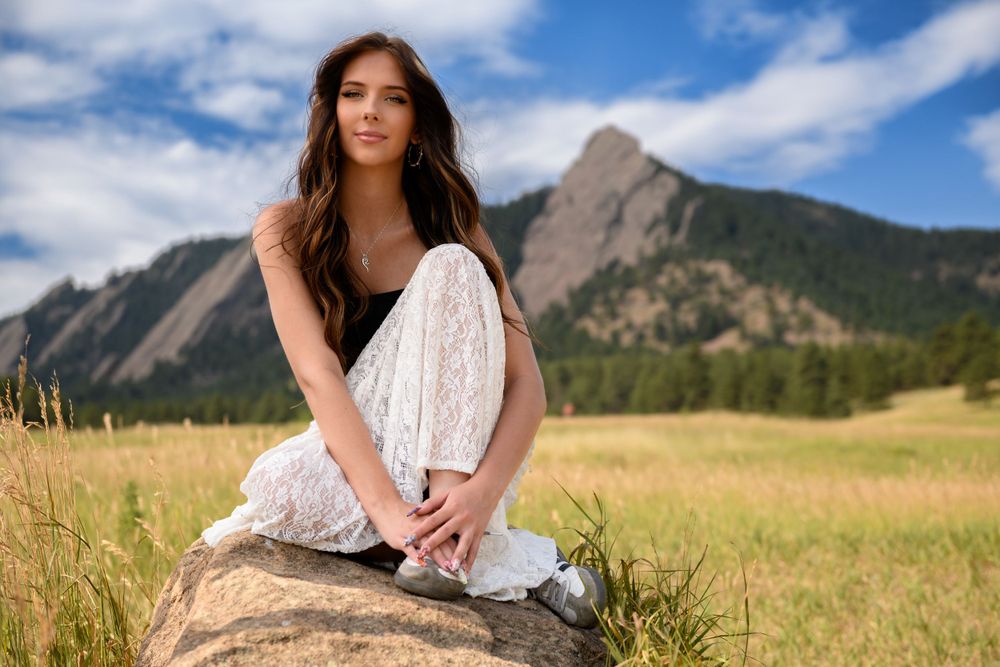 Woman in white dress sitting on rock with mountain landscape in background.