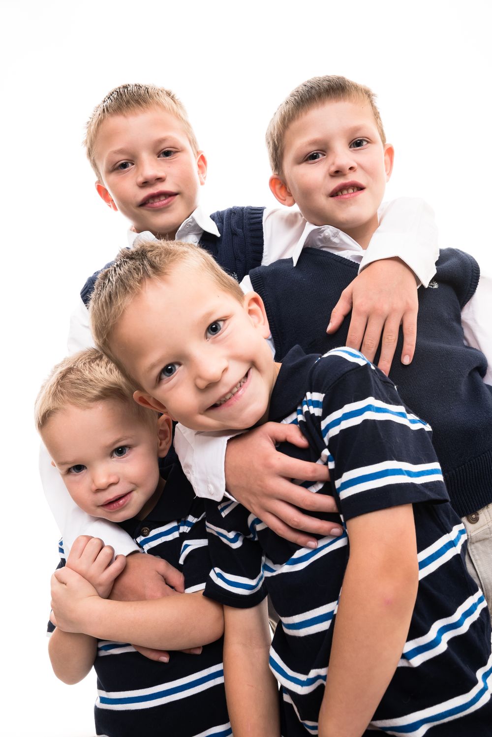 Four young boys in matching striped shirts and dark vests posing together.