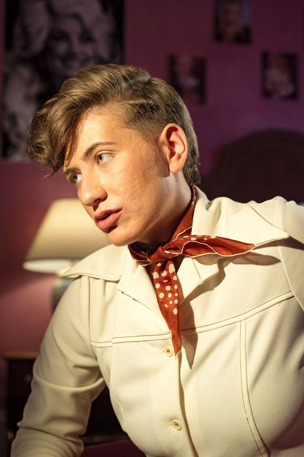 A retro-styled fashion portrait featuring a cream jacket and polka dot neckerchief against a purple background.