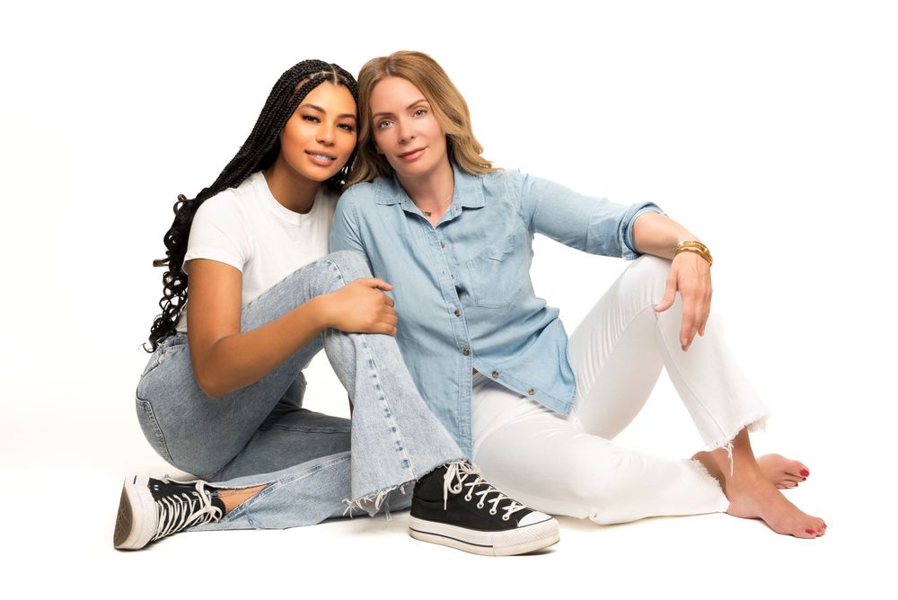 Two friends in casual attire relaxing together against white background.