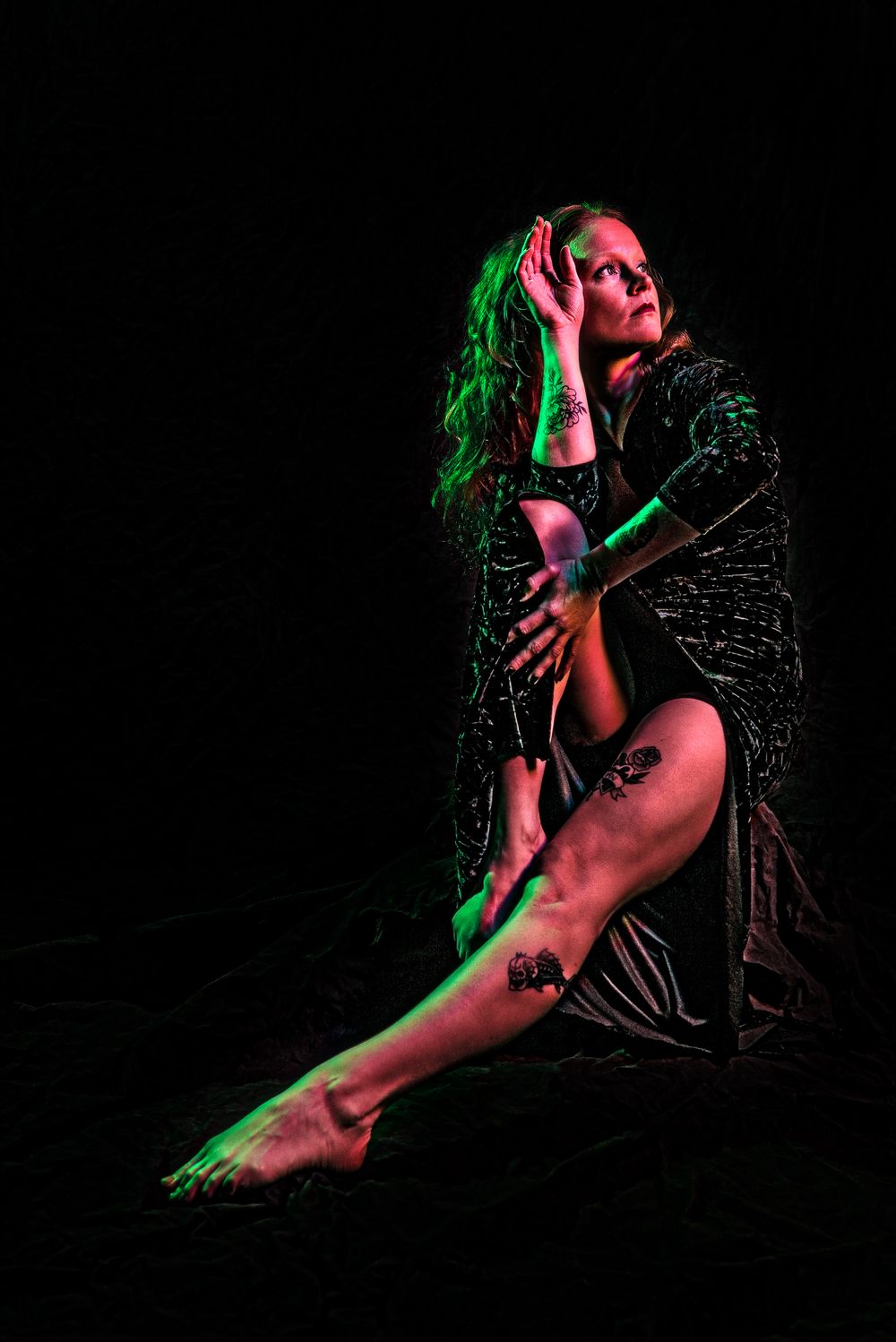 Artistic portrait with dramatic red and green lighting against black background.
