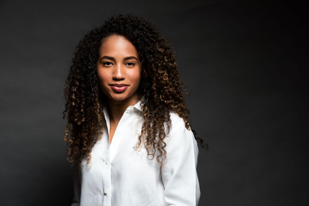 Professional portrait of a woman with curly hair against a dark background wearing a white shirt.