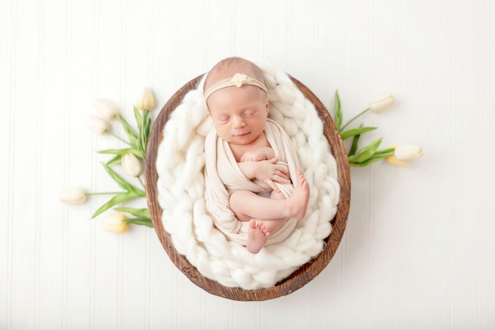 Peaceful sleeping newborn nestled in soft white fabric in wooden bowls with green accents.