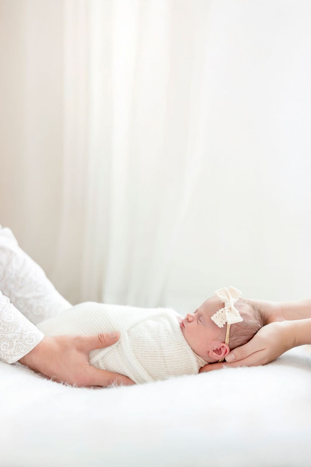 A sleeping newborn baby wrapped in white swaddle cloth lies peacefully on soft white bedding.