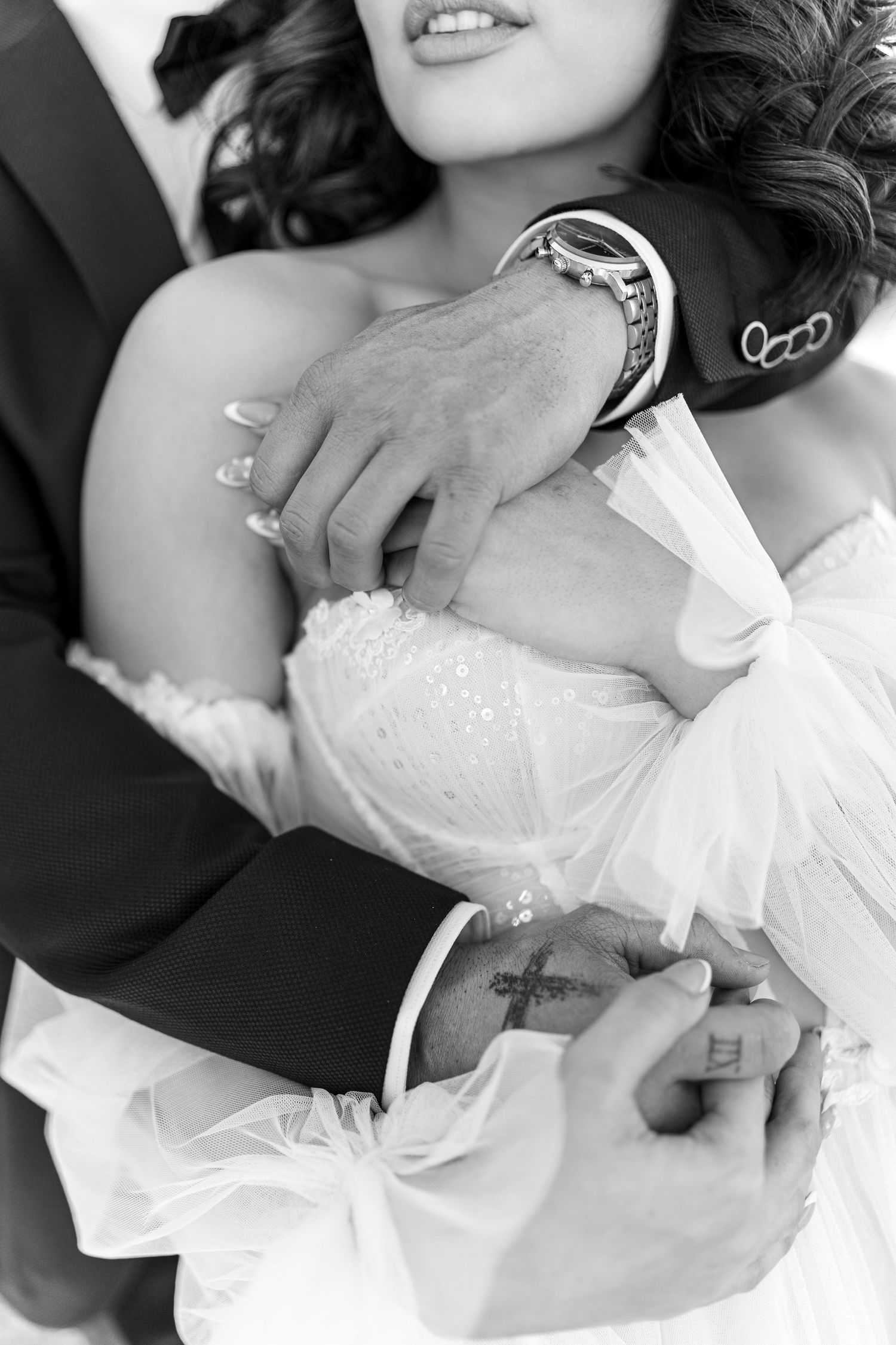 Close-up black and white photo of wedding rings and lace dress details.