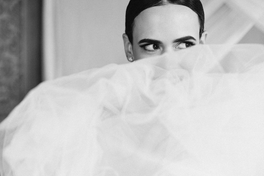 Artistic black and white portrait with white tulle veil covering half the frame.
