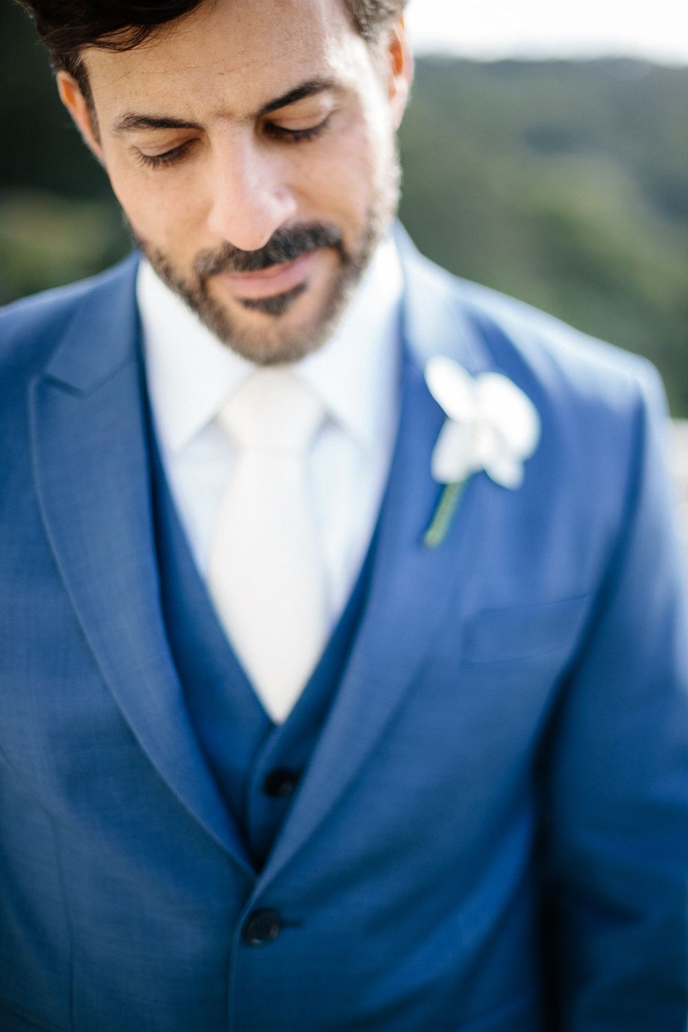 A groom in a tailored blue suit with a white boutonniere shown in close-up detail.