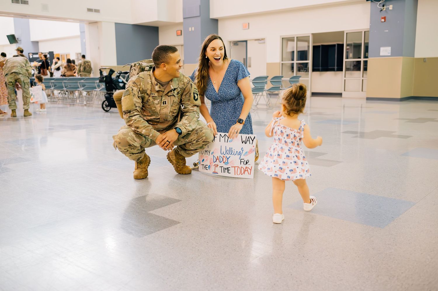 Service member in military uniform crouches down in indoor gathering space.