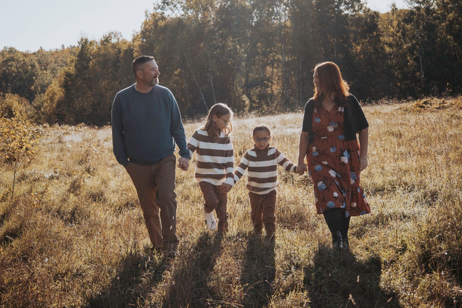 A family enjoying a playful moment together in an autumn forest setting with golden foliage in the background.