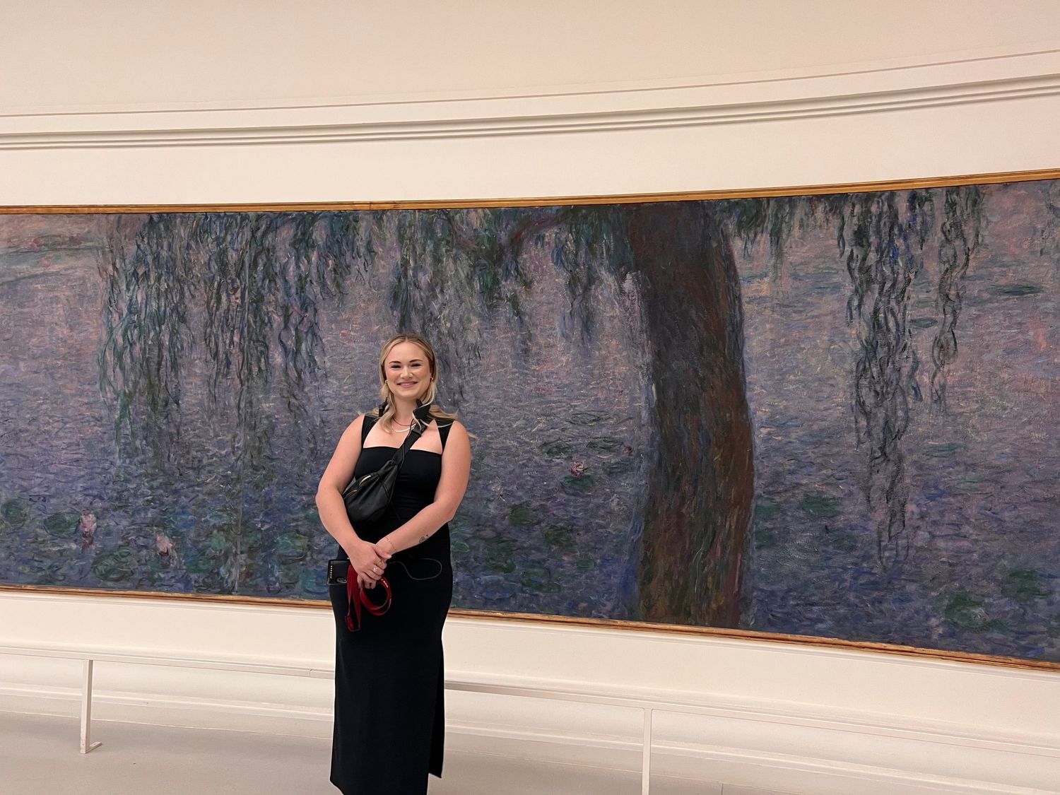 Woman in black dress posing in front of Monet's Water Lilies painting at a museum gallery.