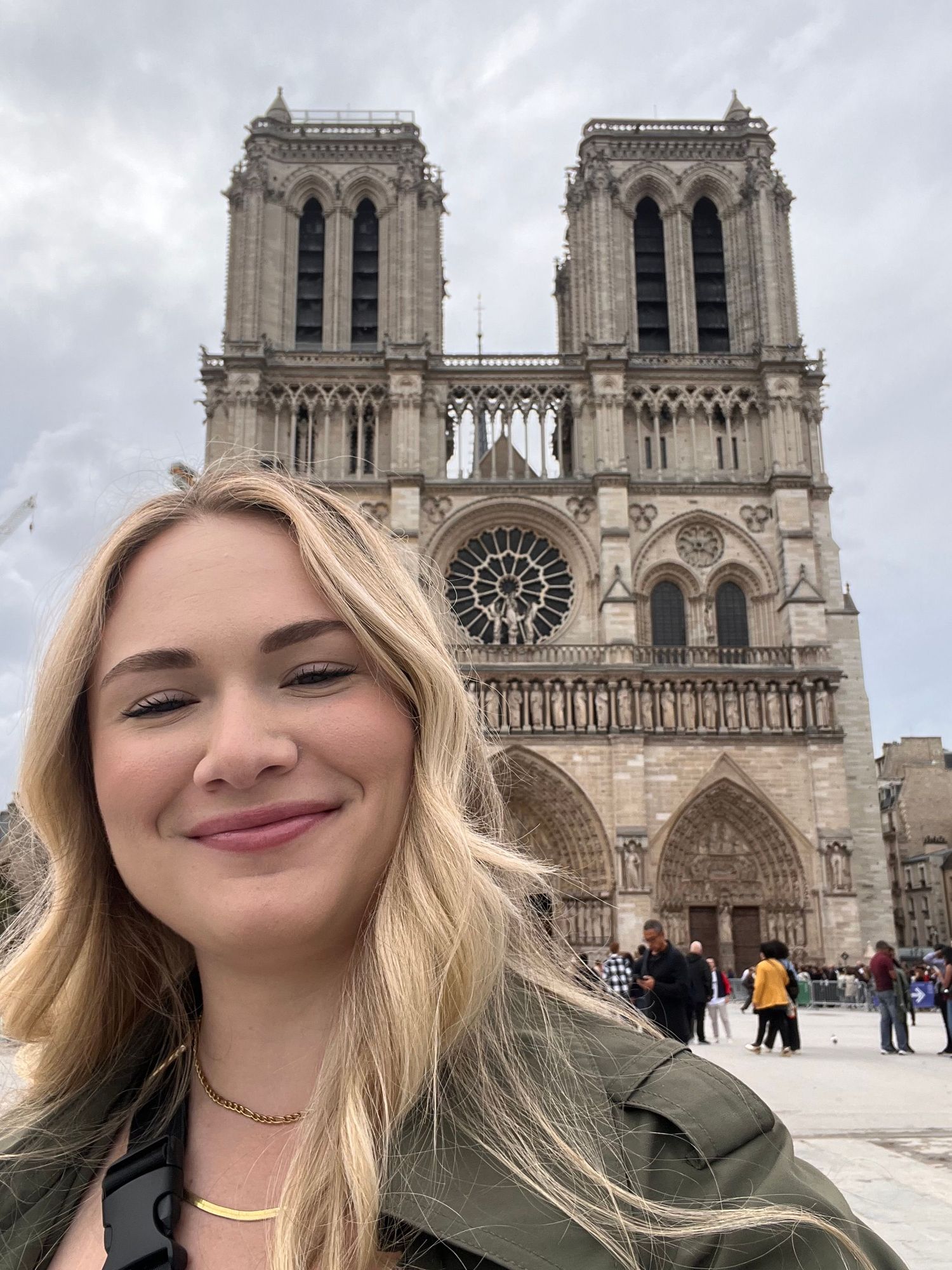 Young woman smiling in front of Notre-Dame Cathedral in Paris, France, with Gothic architecture visible behind her.