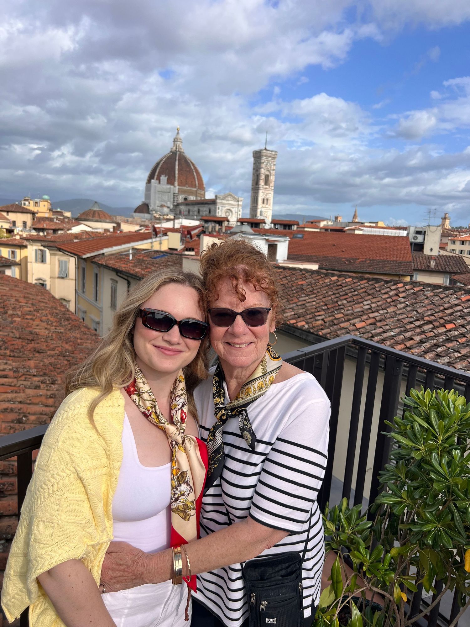 Two women posing on a rooftop terrace in Florence, Italy, with the iconic Duomo cathedral in the background.