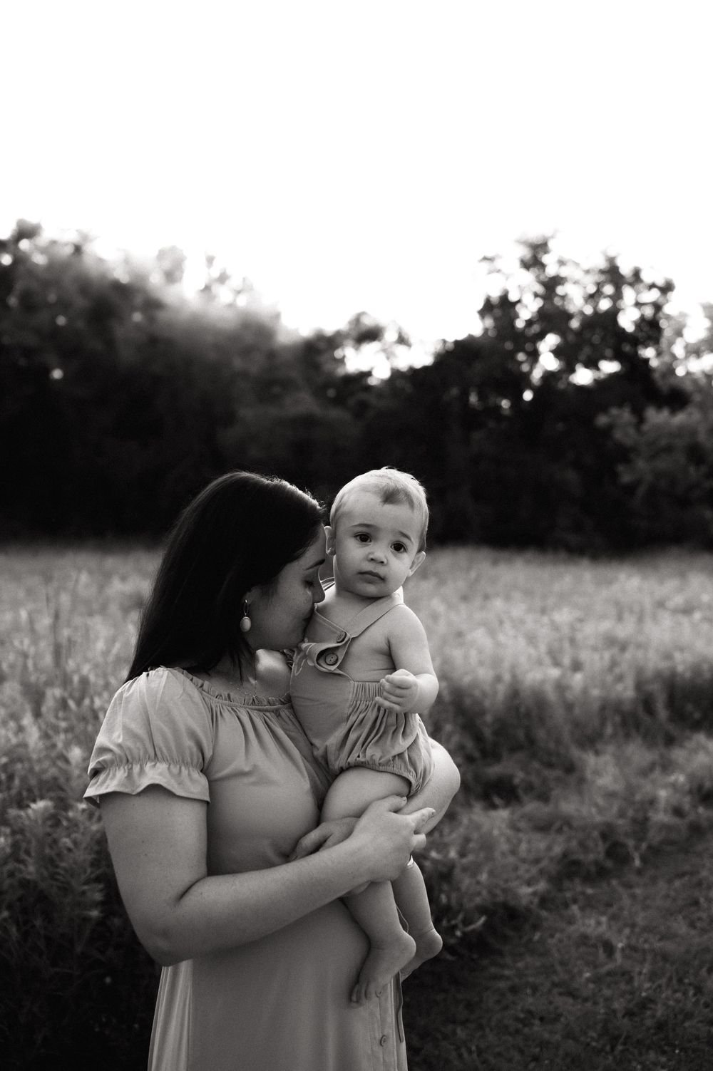 A tender moment between a parent and baby captured in black and white outdoors at sunset.