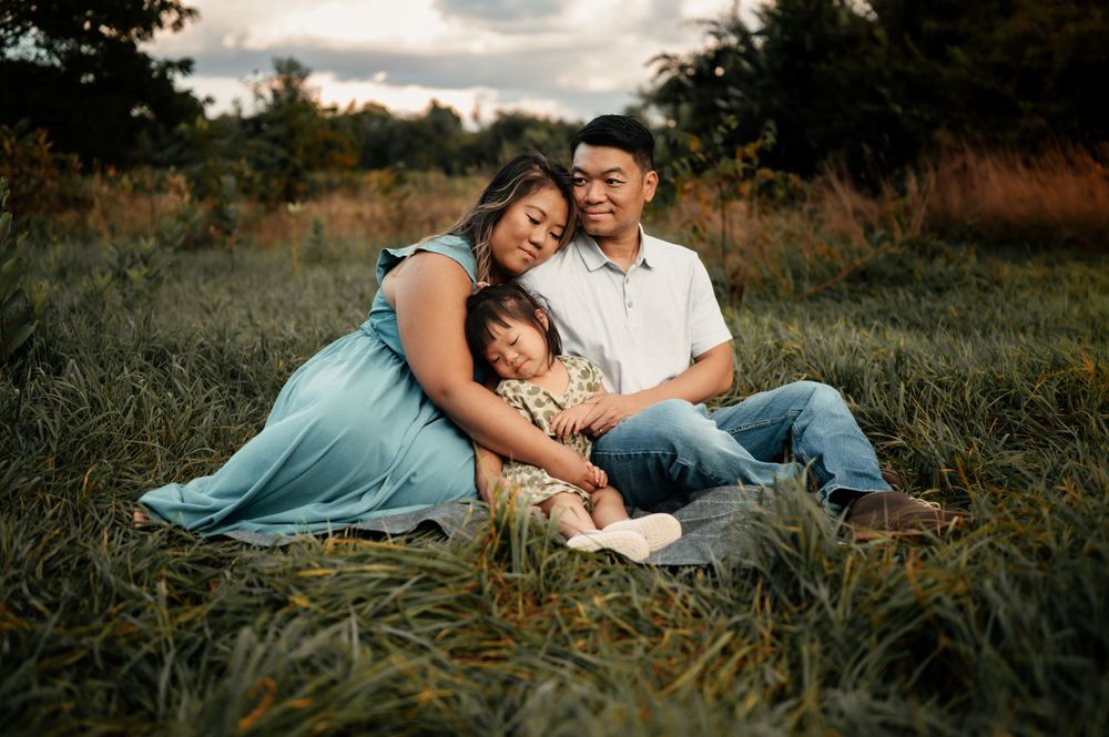 A family shares an intimate moment together while sitting on a blanket in a grassy field at sunset.