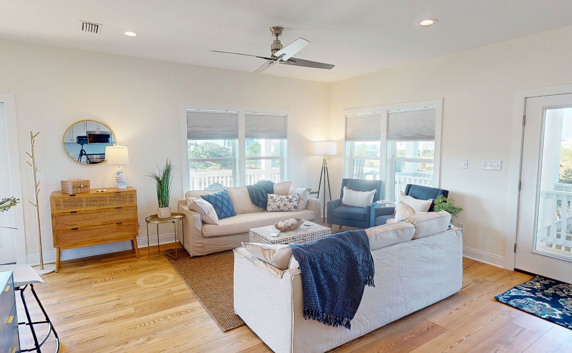 Modern coastal living room with white sofas, blue accents, and natural light streaming through windows.