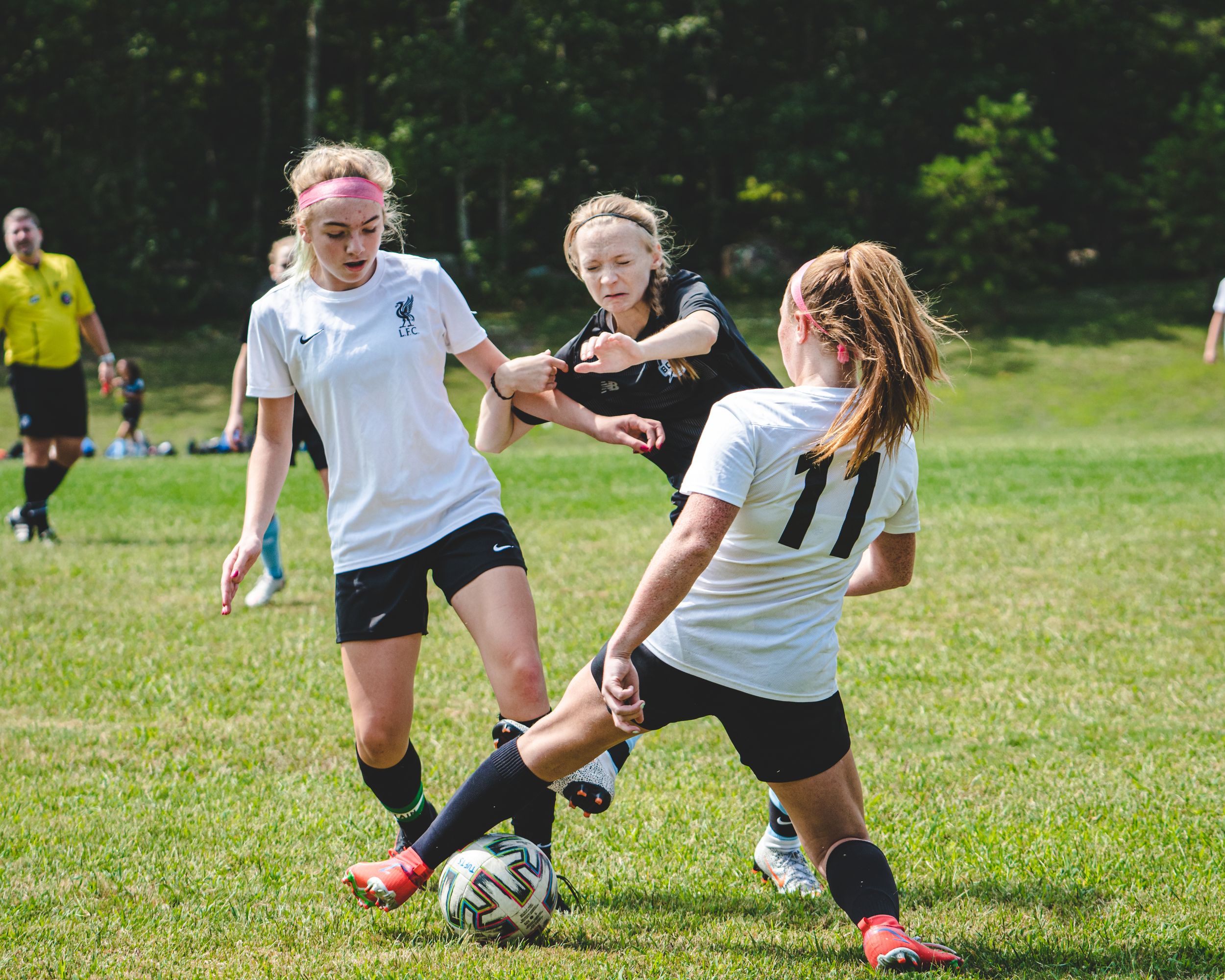 Three girls compete for soccer ball possession during an outdoor youth league game.