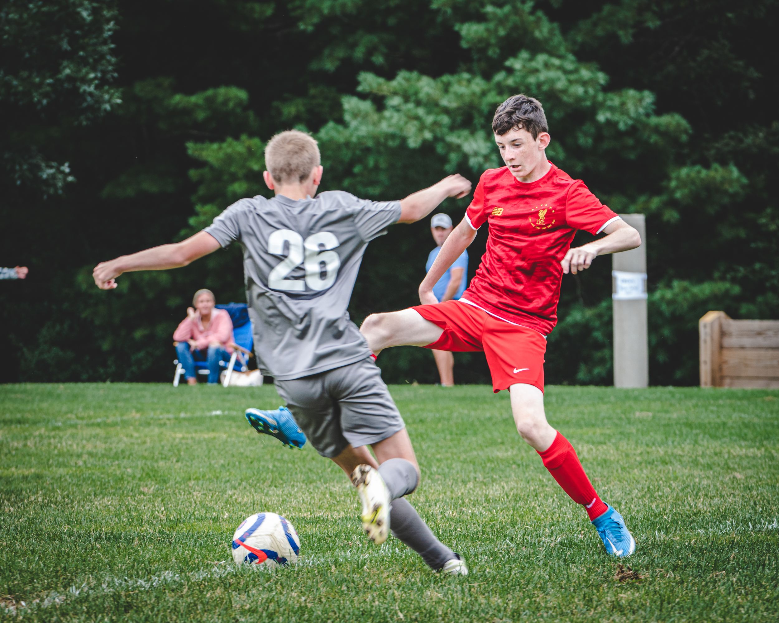Two boys compete in a youth soccer match, with player number 26 defending against a red-uniformed attacker.