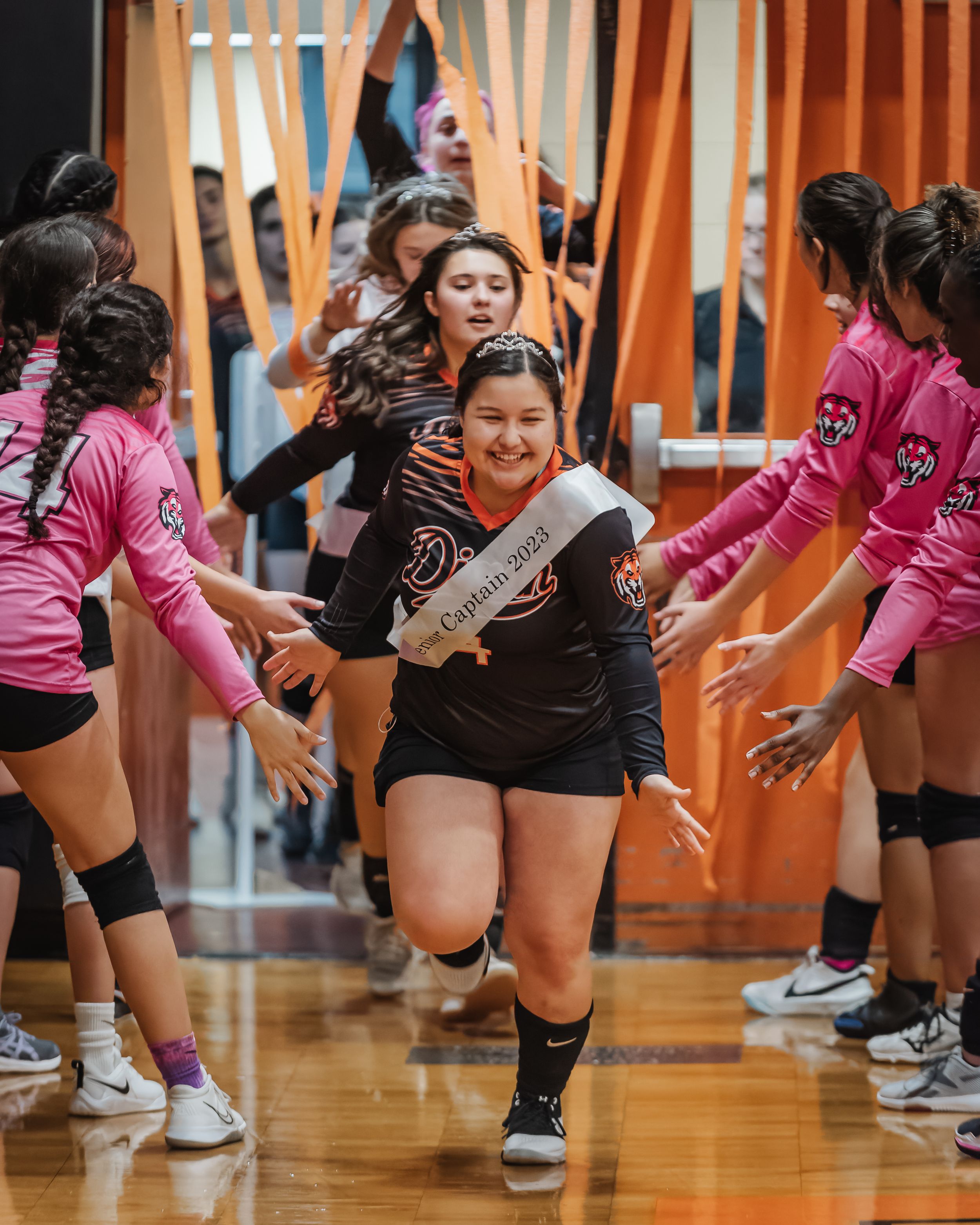 Volleyball team captain runs through player tunnel during pre-game introduction ceremony indoors.