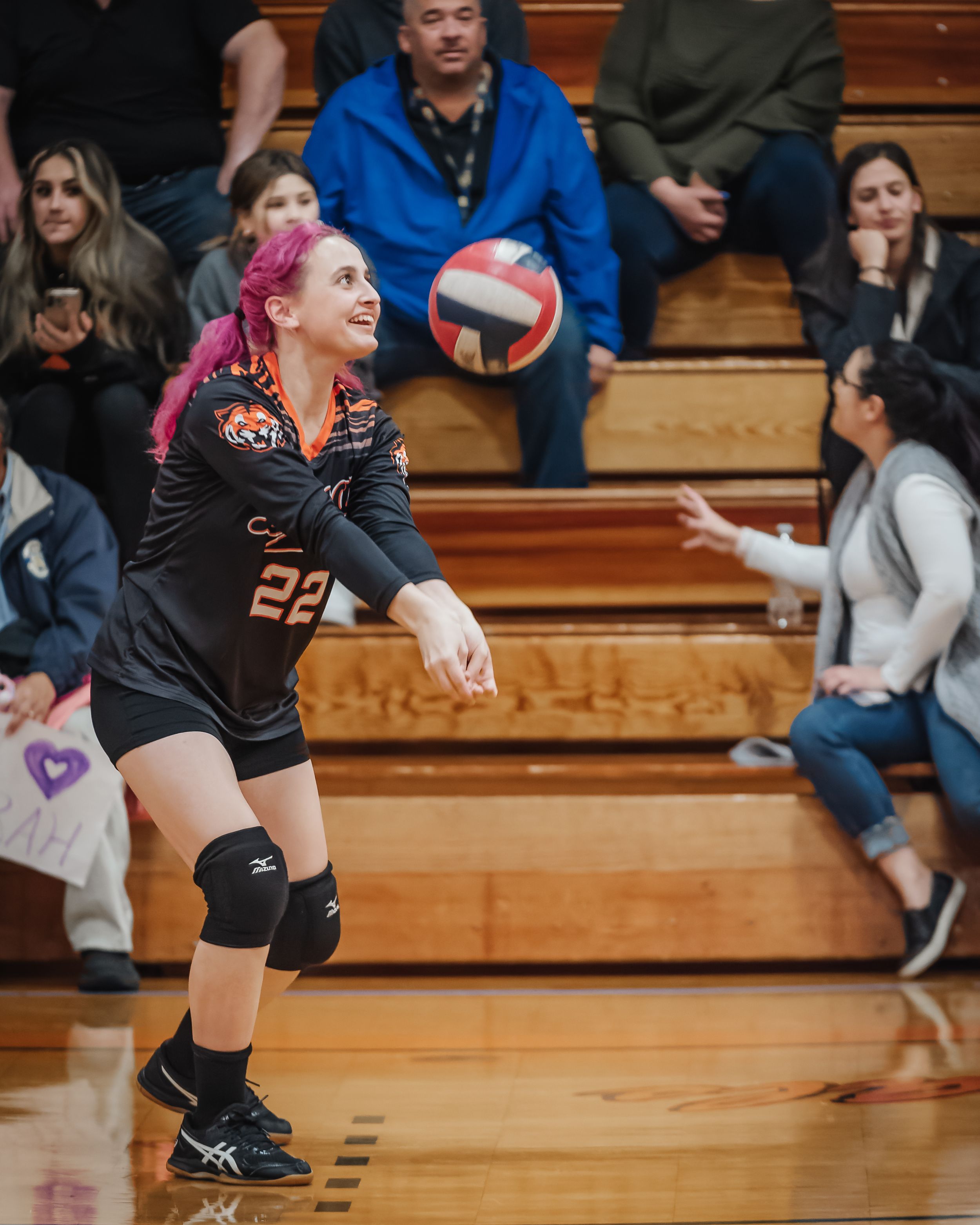 Female volleyball player with pink hair prepares to receive ball during indoor game.