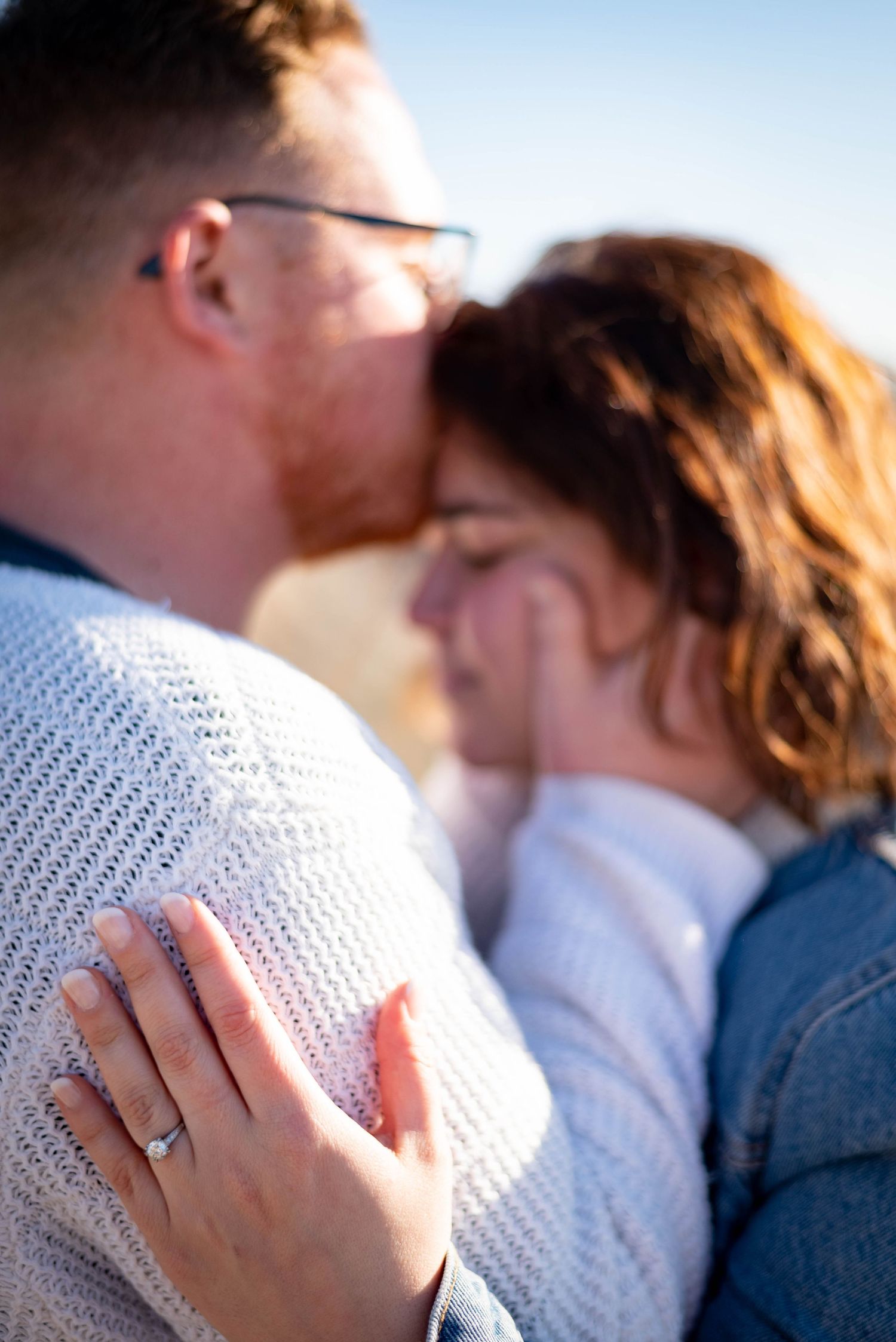 Romantic engagement photography in Orange County featuring a close-up of a couple embracing with an engagement ring visible. Natural, candid