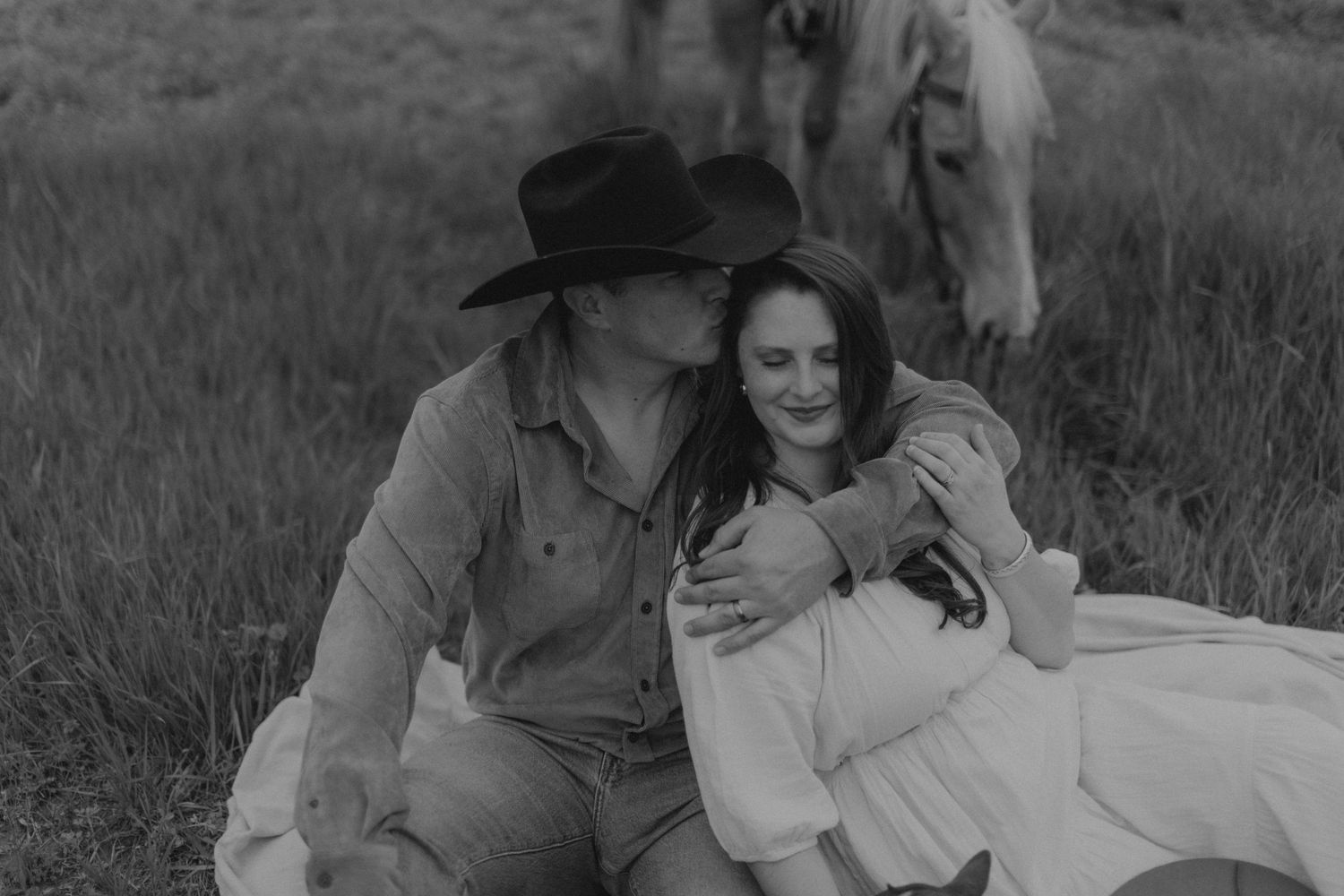 A loving couple shares tender moments in black and white photos taken outdoors in tall grass.