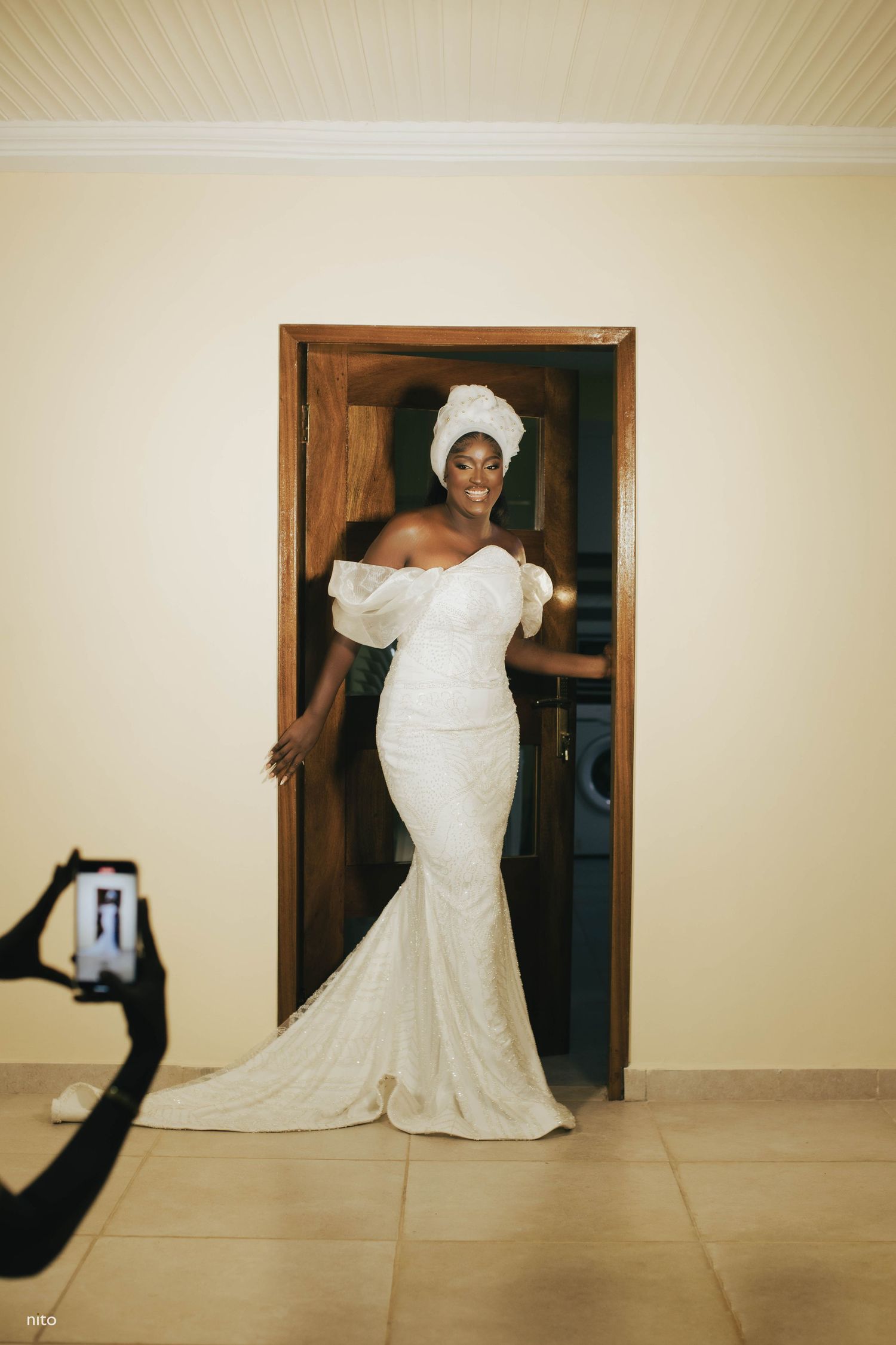Person in fitted white wedding dress poses gracefully against wooden doorframe.