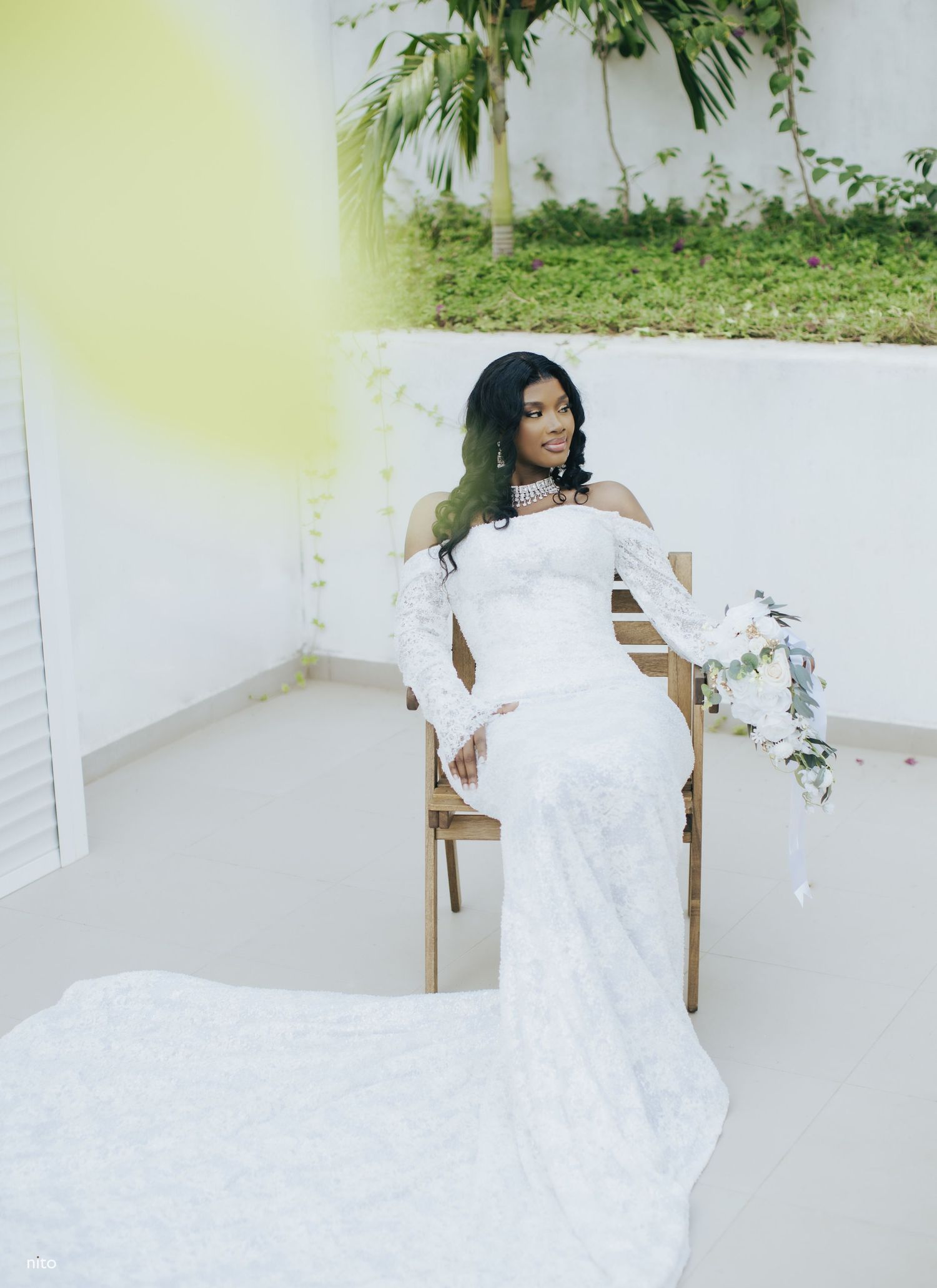 A stunning off-shoulder white lace wedding gown with long sleeves and a flowing train is styled for a bridal portrait.