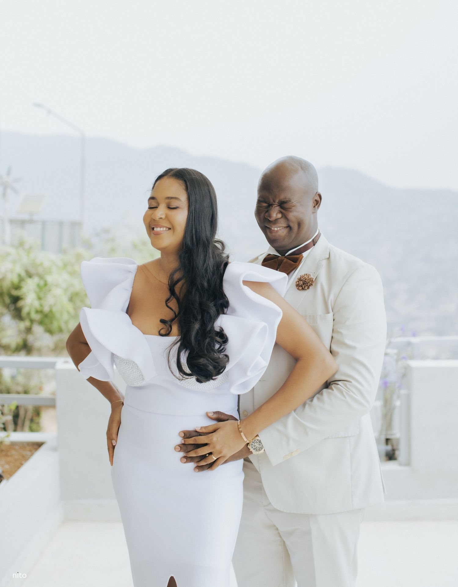 A couple in white attire sharing a romantic moment on a balcony with mountain views.