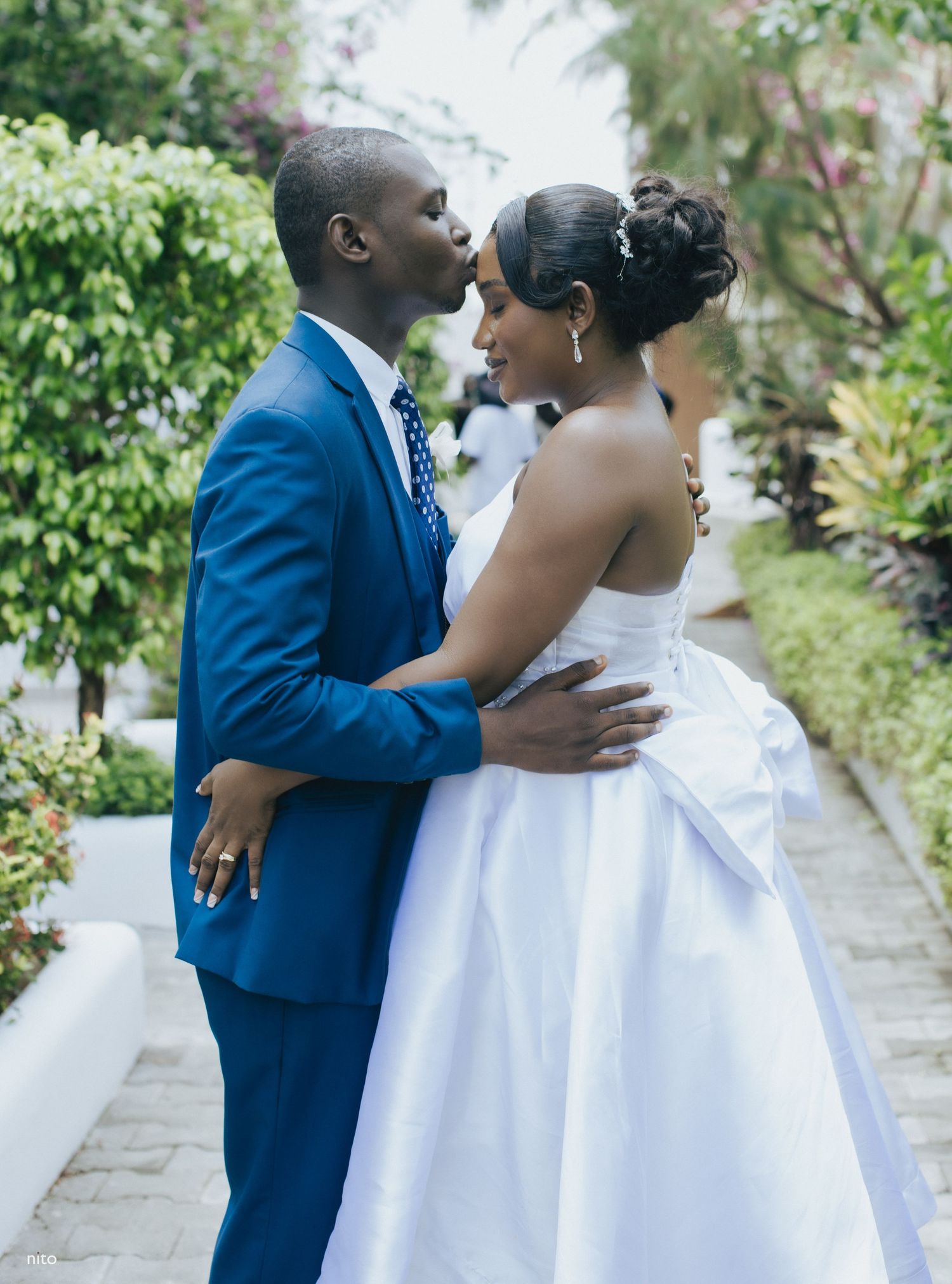 Joyful couple shares intimate moment on garden pathway during wedding celebration.