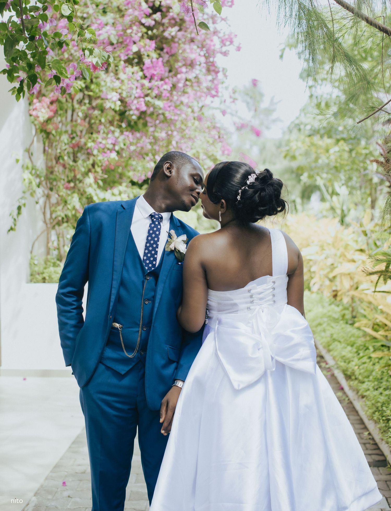 Wedding couple shares romantic moment in garden setting with blooming flowers.