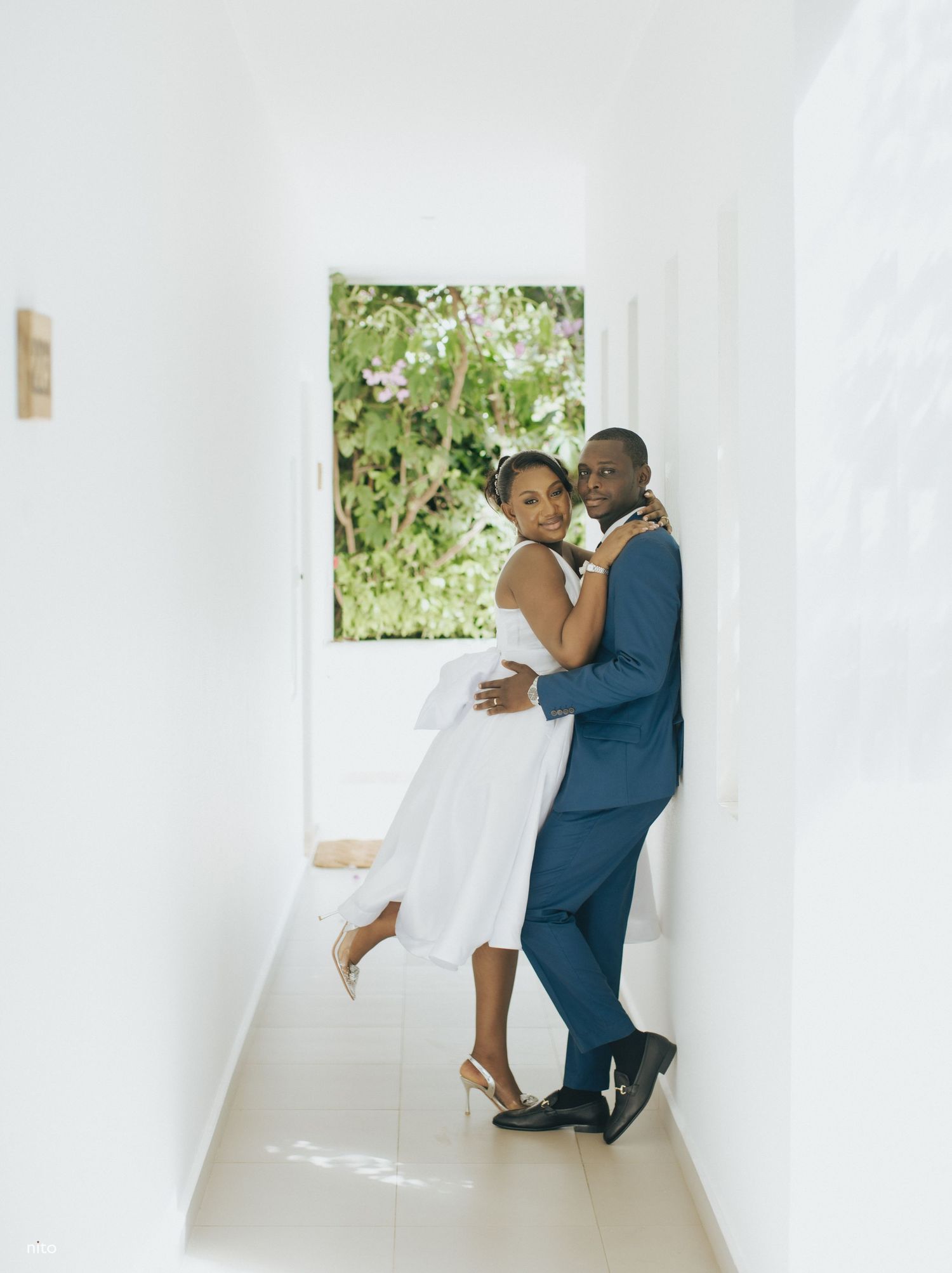 Romantic couple embraces in white hallway during wedding photoshoot.
