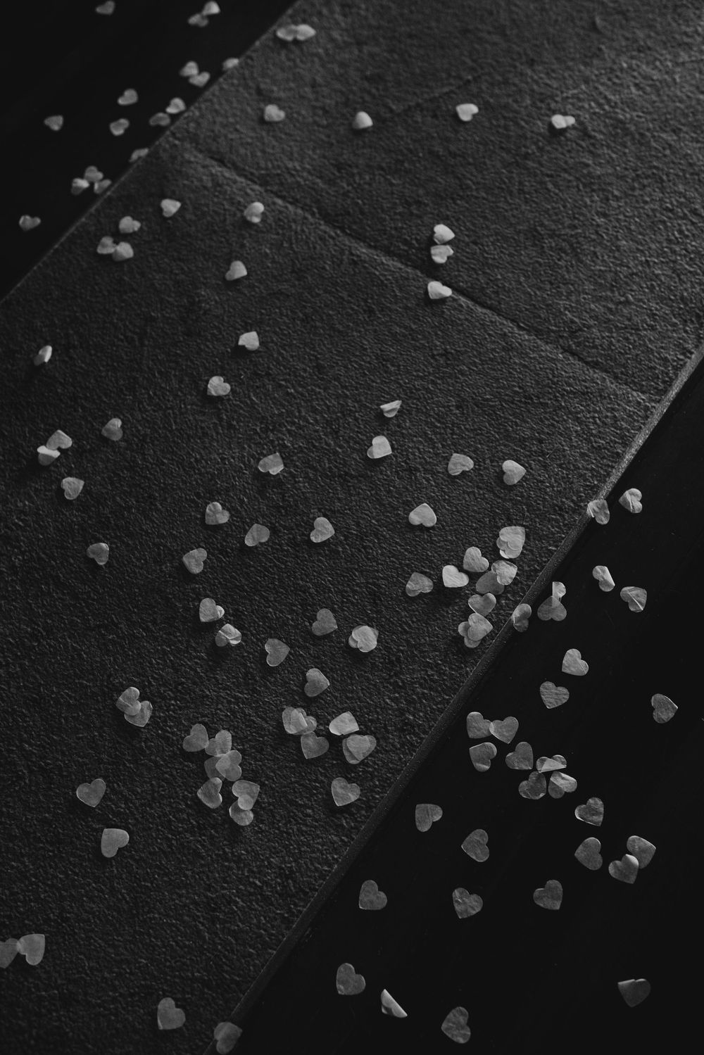 Close-up black and white photo of heart-shaped confetti scattered on dark textured surfaces.