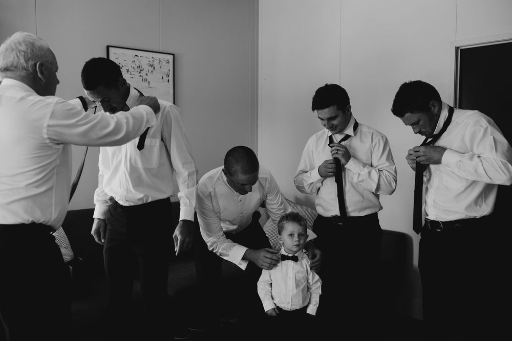 Black and white photo of groomsmen helping each other with ties while a young boy watches.