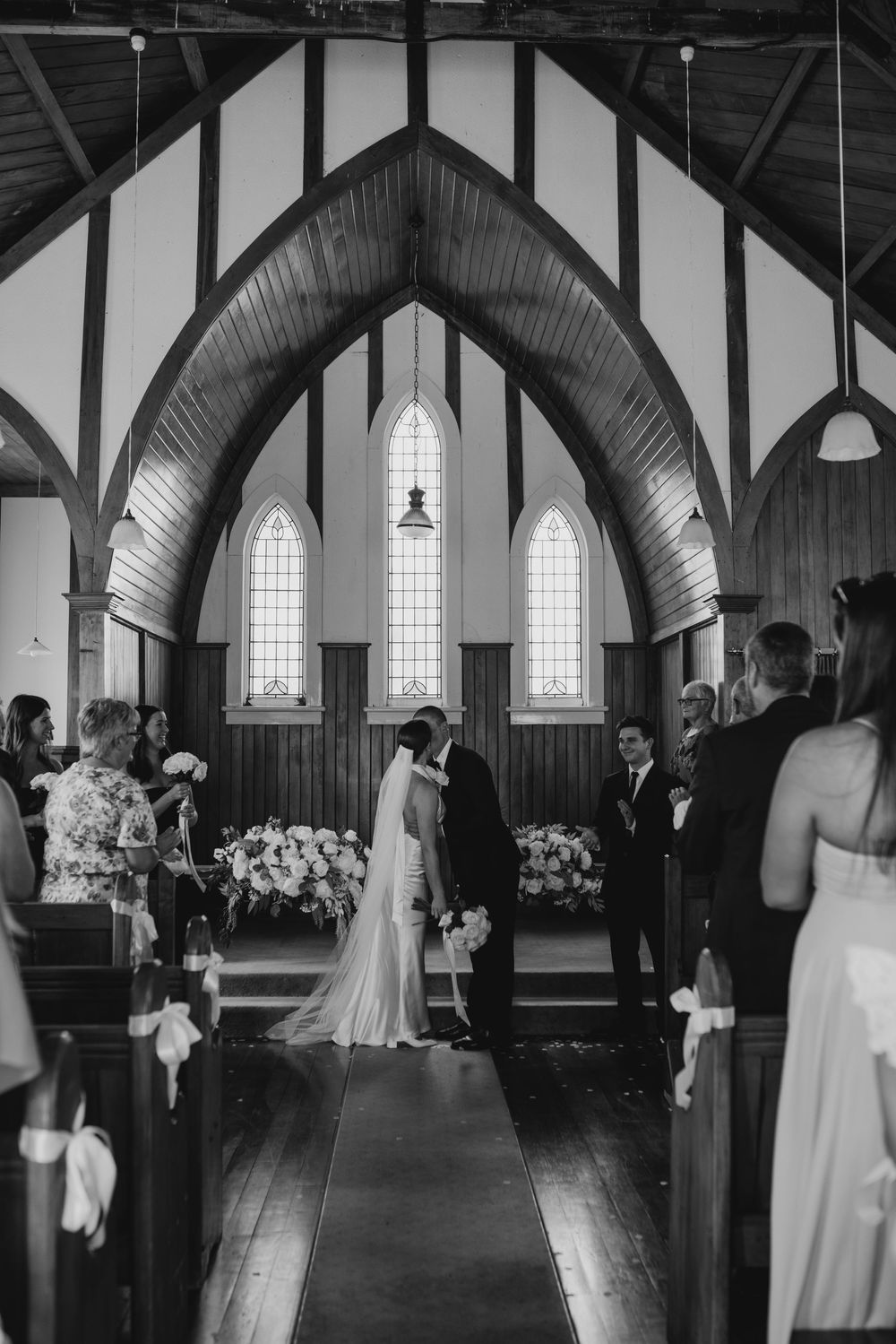 Black and white photo of bride and groom sharing first kiss at altar in a beautiful wooden church.