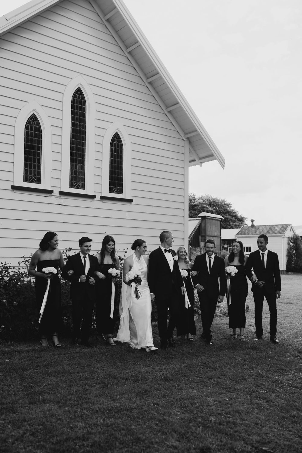 Wedding party walking together outside a white historic chapel on a cloudy day.