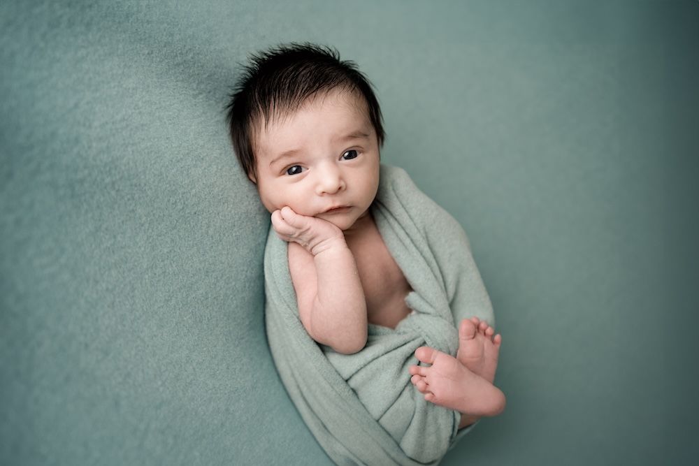 Newborn boy swaddled with his hand under his chin