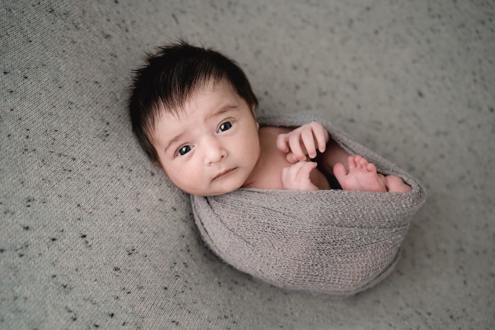 Newborn boy swaddled in grey on his back