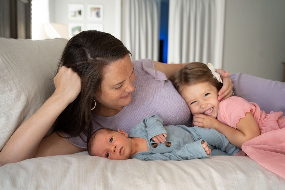 A mom, new newborn and toddler cuddling on a bed