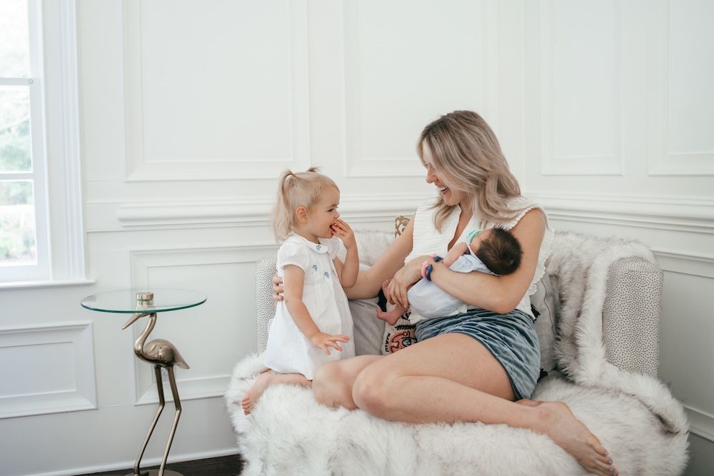 Mom, newborn baby and toddler daughter sitting on a chair chatting