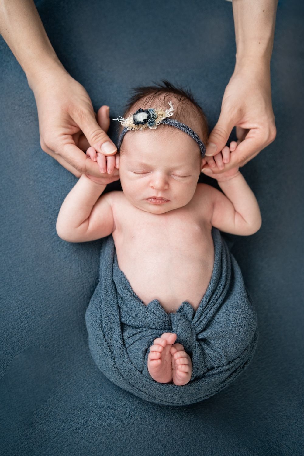 Newborn baby wrapped in blue with her mom holding her hands