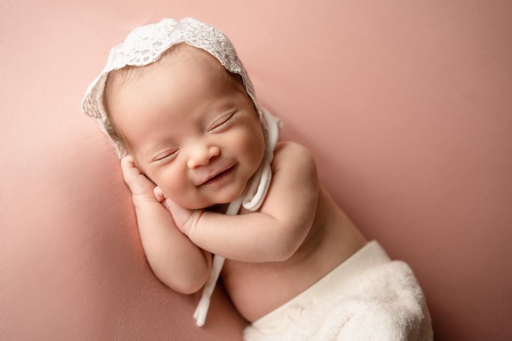 Baby girl on a pink backdrop wearing a lace bonnett
