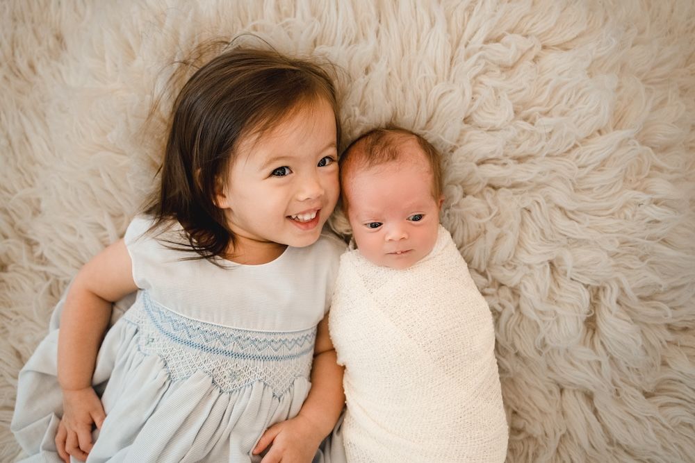 Newborn baby and older sister laying on a rug