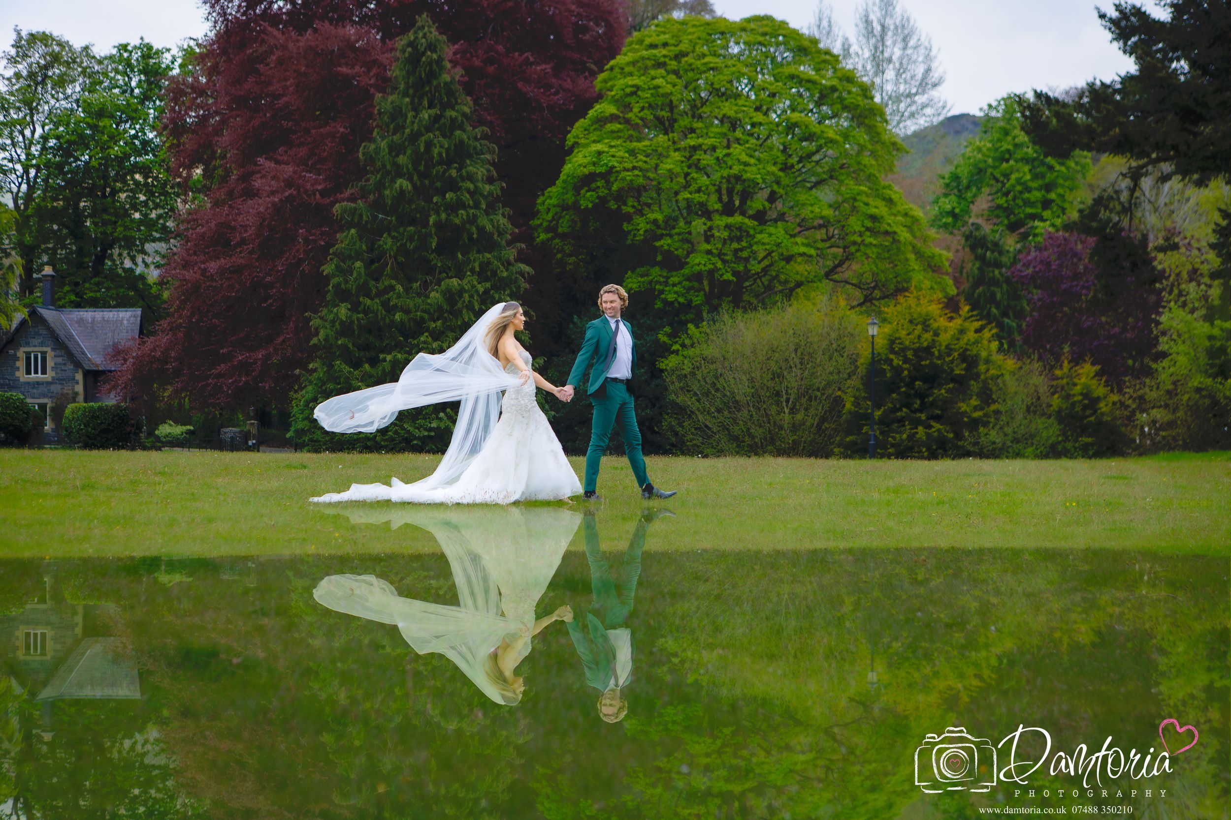 Bride and groom walking hand in hand on lush green lawn with stunning reflection in water at outdoor wedding.