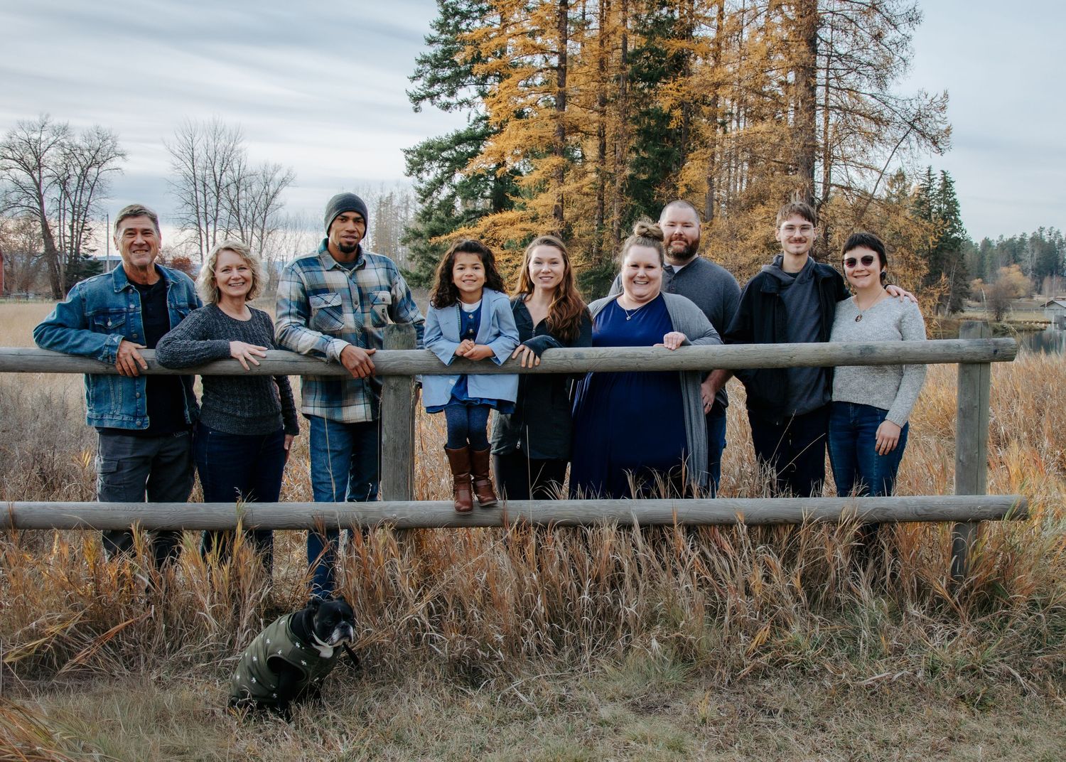 Group of people gathered outdoors in autumn wearing casual clothing pose together on a grassy hillside.