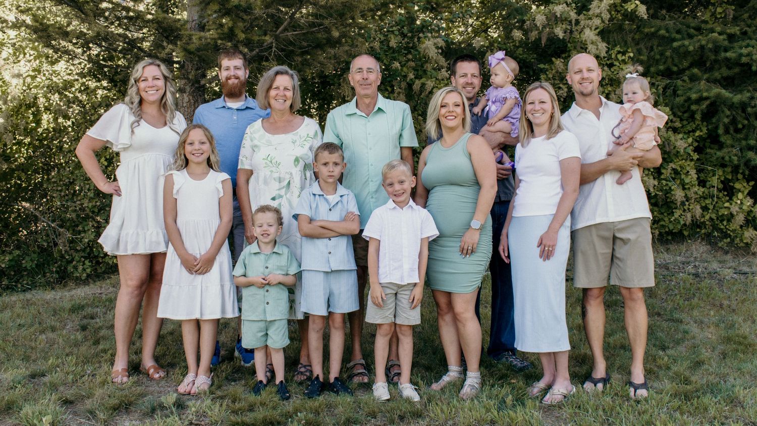 A group in coordinated blue and white outfits poses together outdoors for a family portrait in a garden setting.