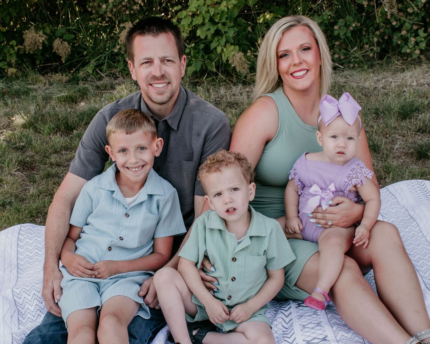 A family sits together outdoors on a blanket wearing coordinating mint green and neutral colored outfits for photos.