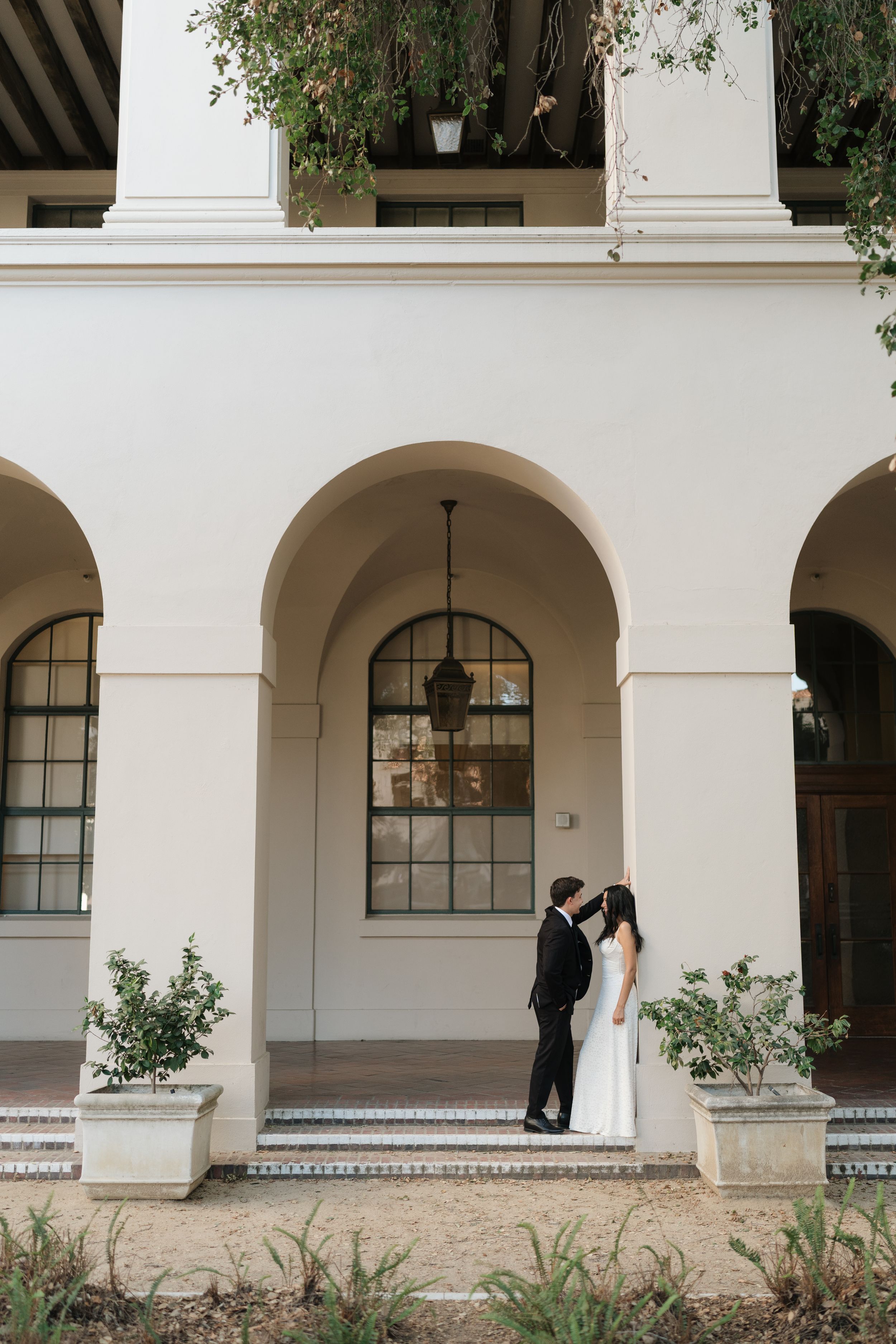 Engagement Session couple share an intimate moment beneath arched white columns of an elegant venue exterior. Fresno California Wedding